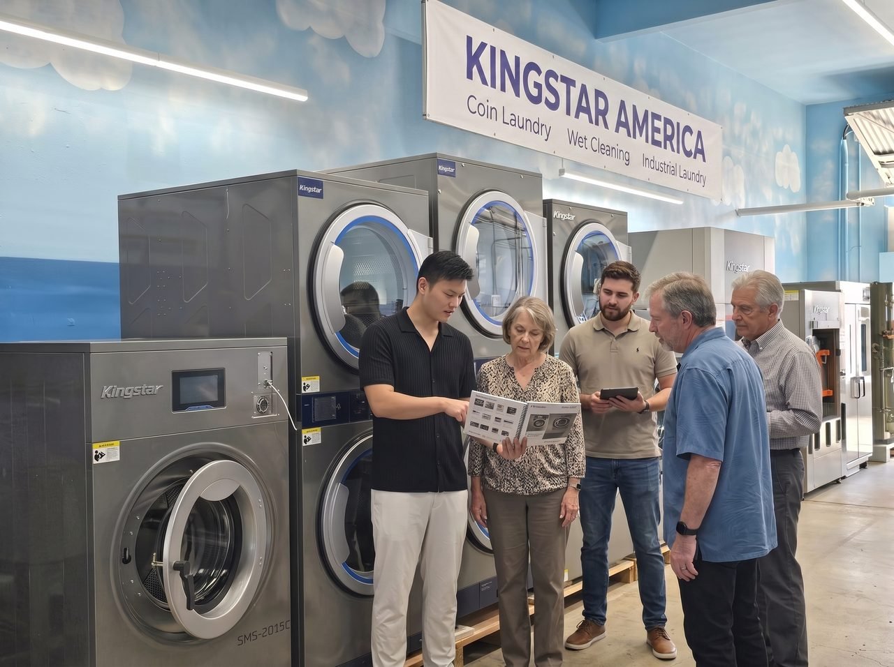 Kingstar America staff walking laundry owners through the equipment catalogue on the showroom floor, in front of stacked washer-dryers and an SMS-2015C coin washer.